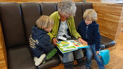 Lesepaten: Frau liest zwei Kindern vor, in der Schulbibliothek